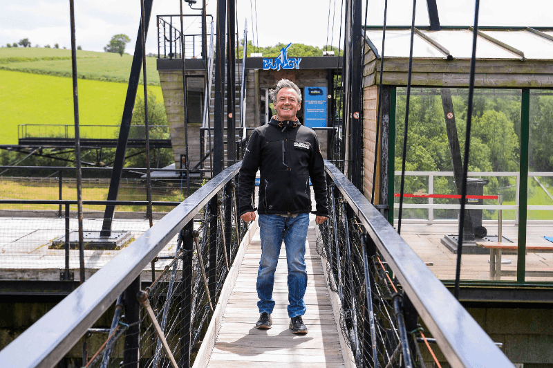 AJ Hackett walking towards the camera with a smile at one of the Skypark sites, exuding excitement and joy.